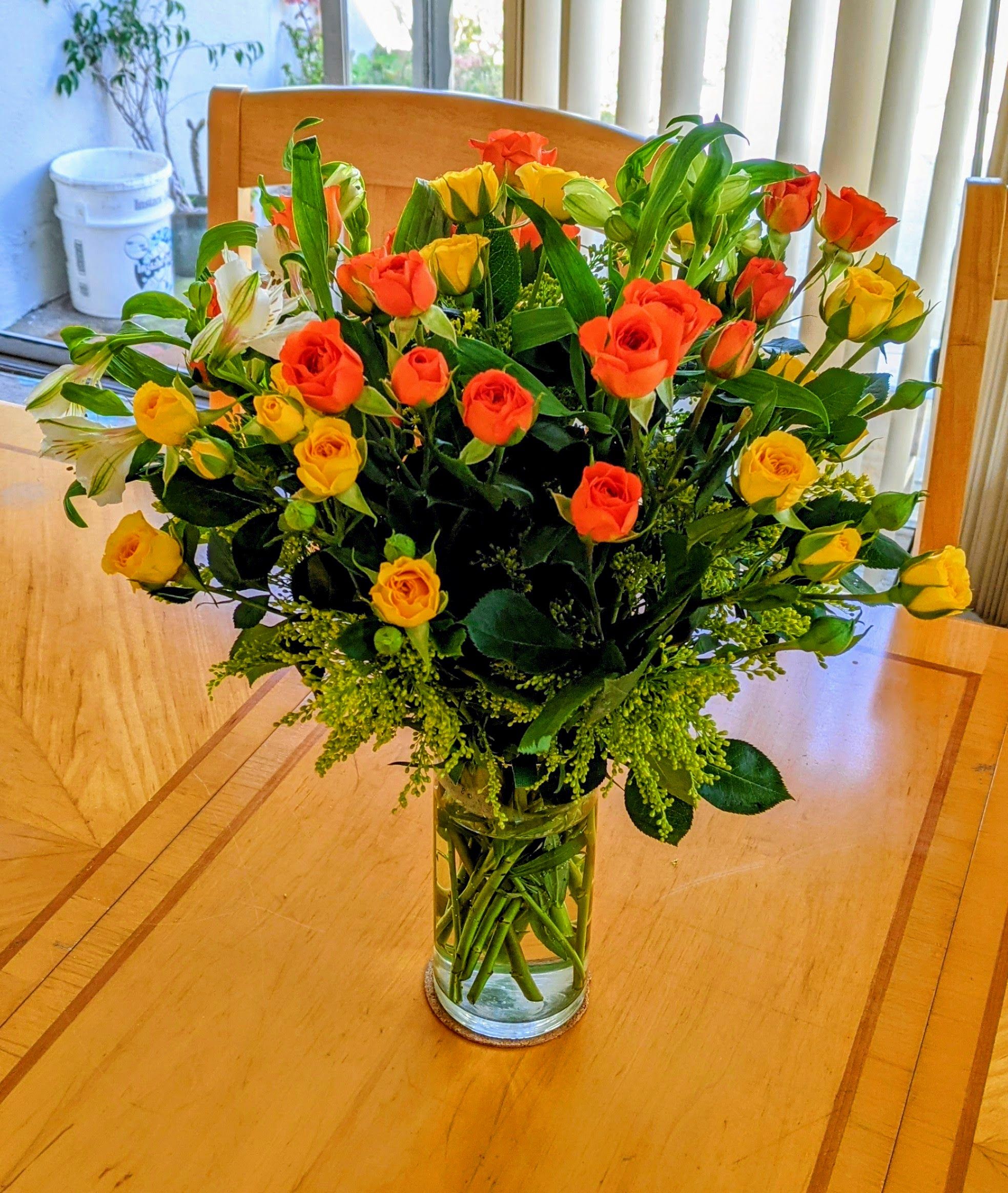 Orange roses and greens in a clear vase